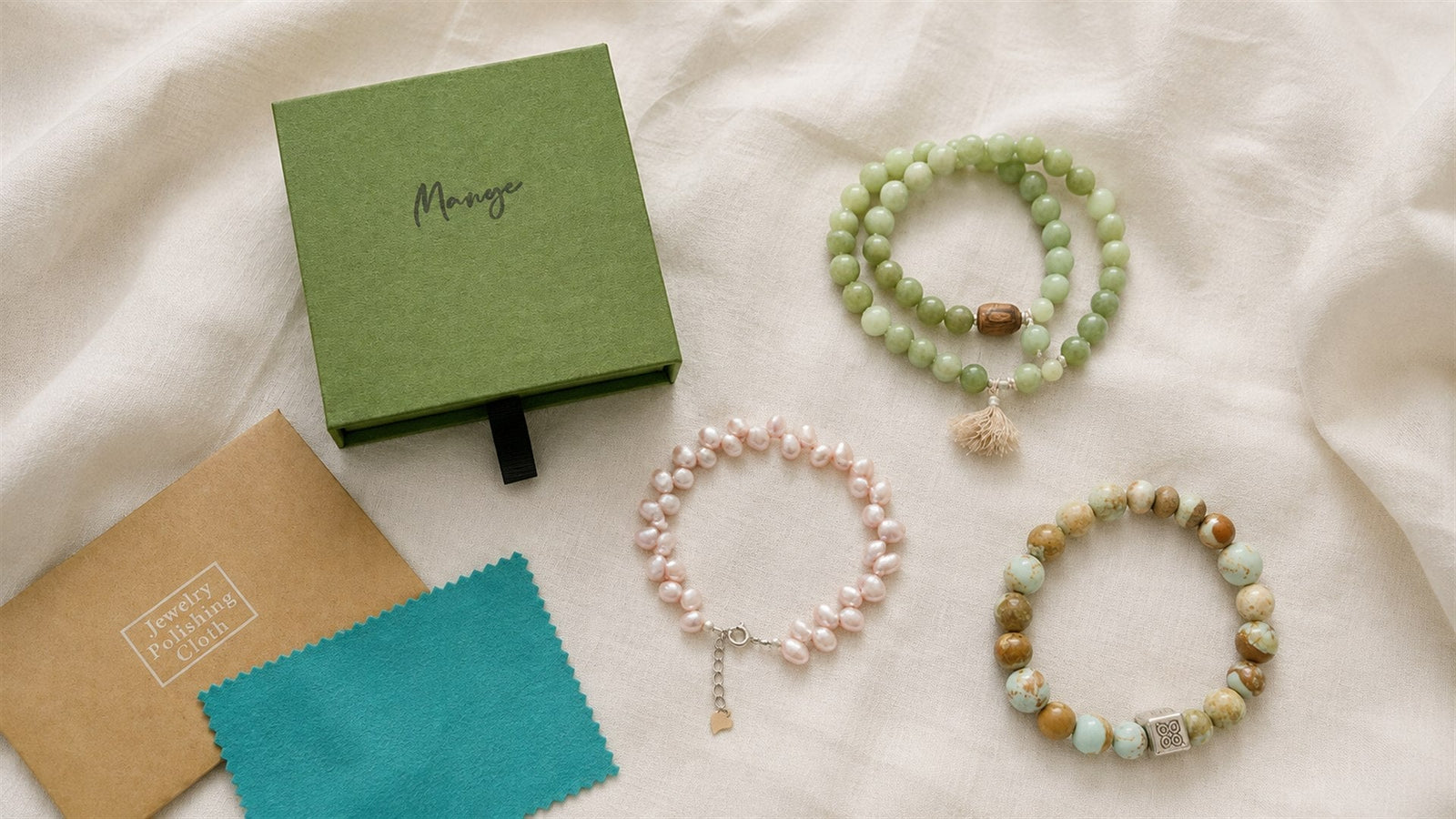 Natural-stone and pearl bracelets with jewelry-care supplies on ivory linen