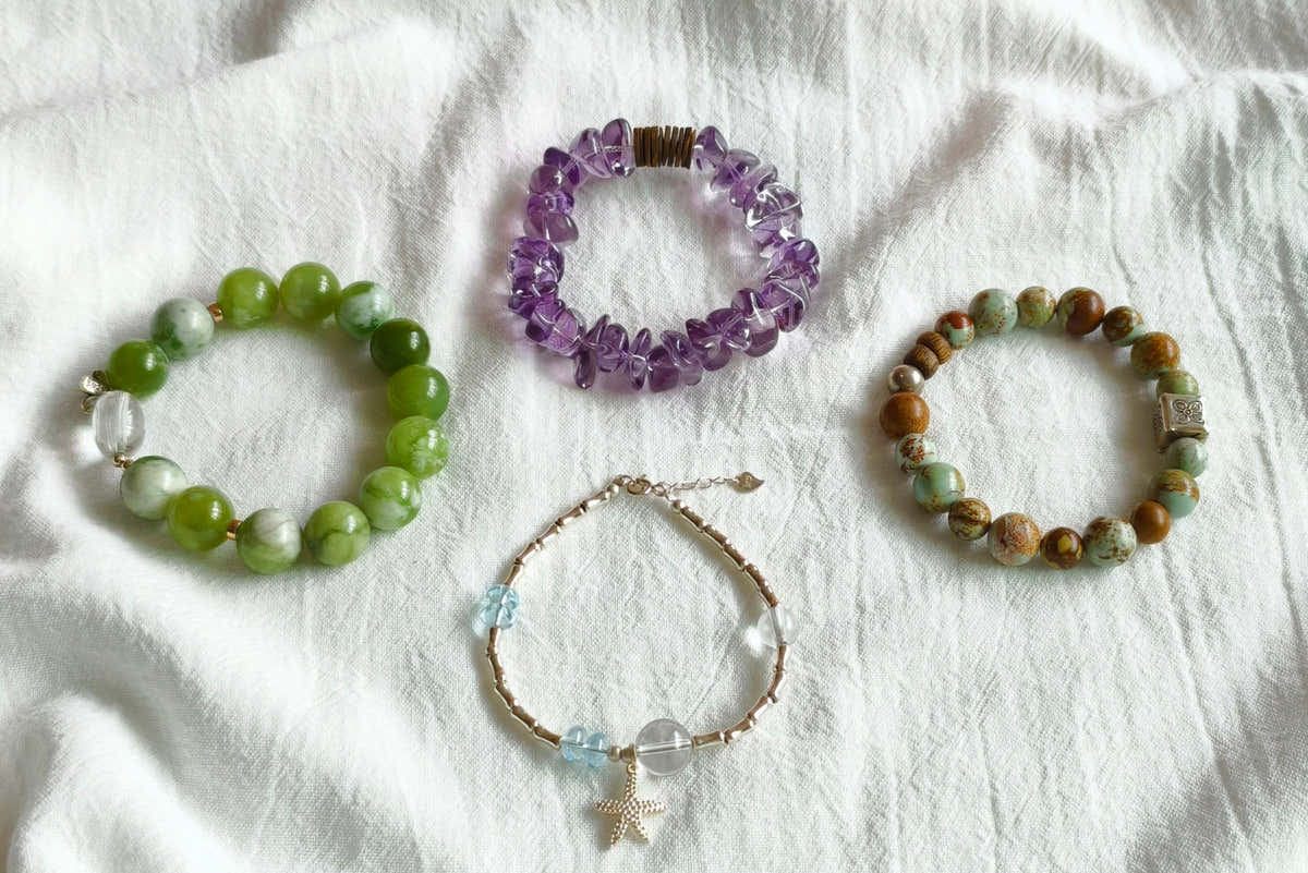 Four handmade gemstone bracelets in green jade, purple amethyst, picture jasper and blue topaz on white fabric