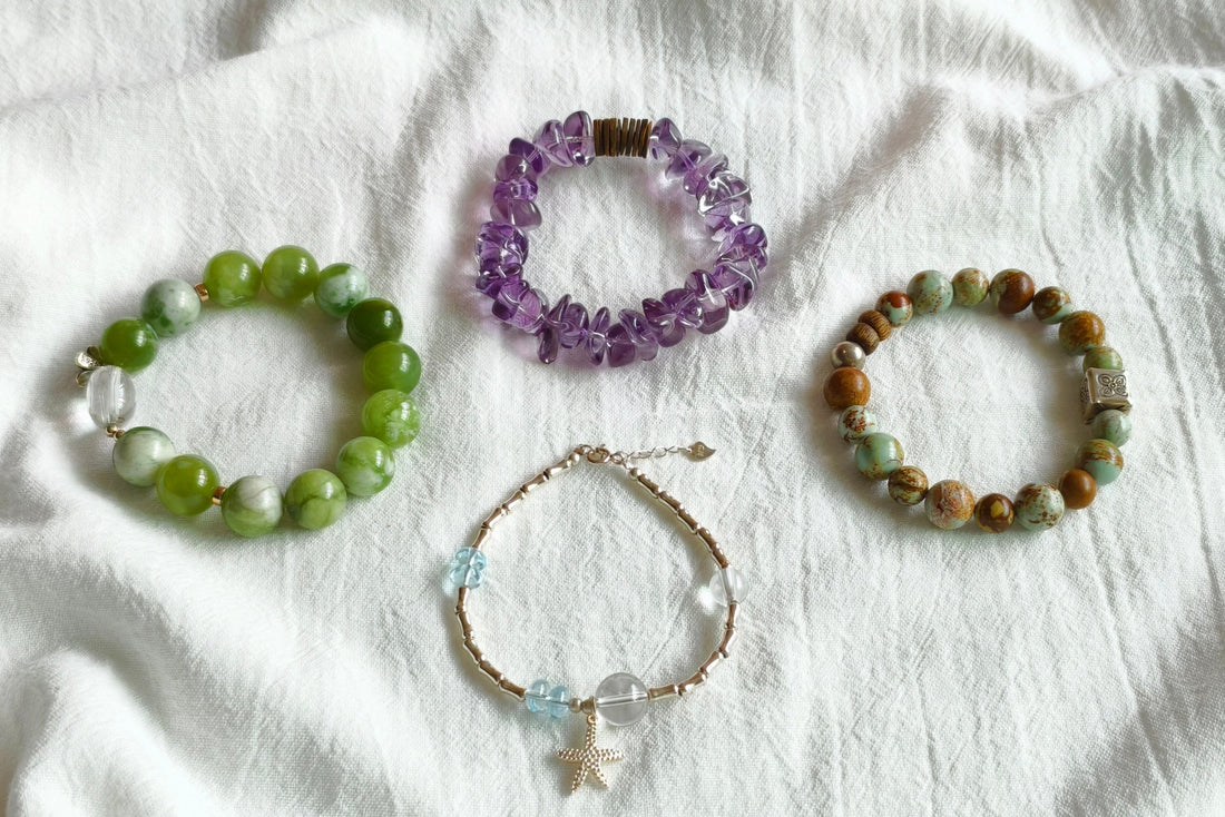 Four handmade gemstone bracelets in green jade, purple amethyst, picture jasper and blue topaz on white fabric