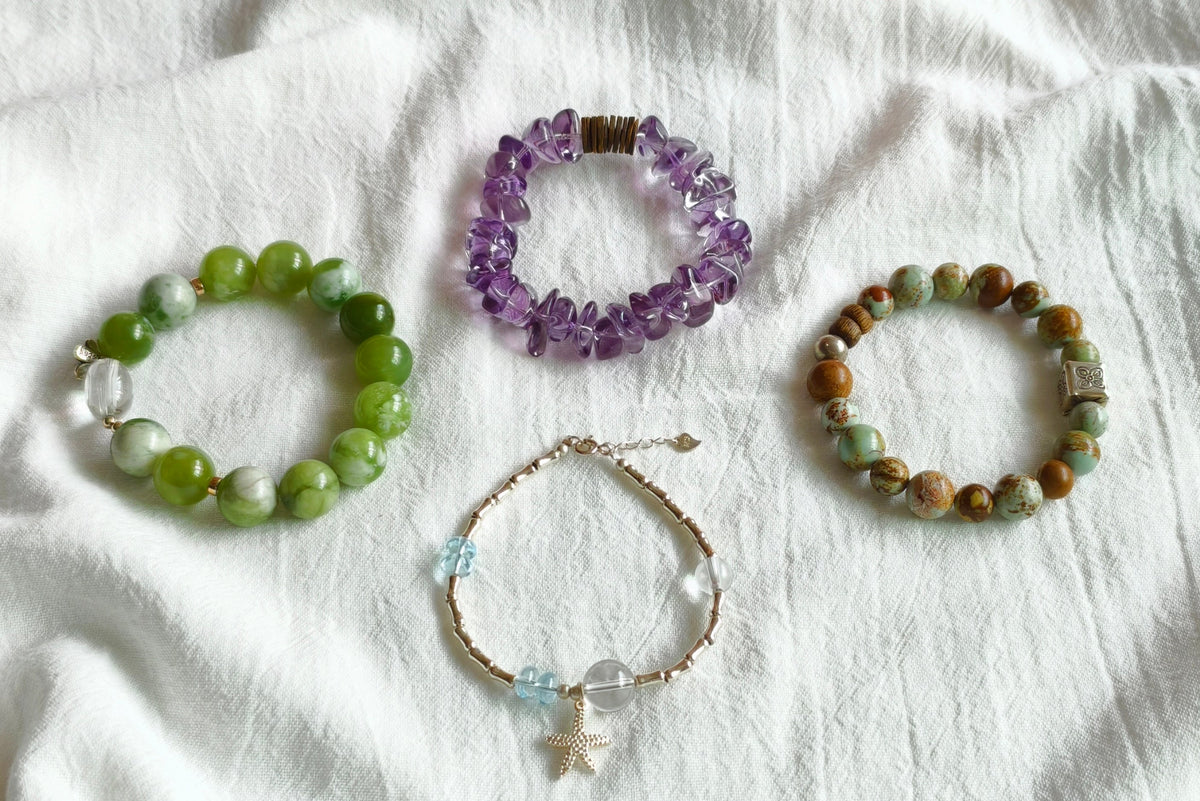 Four handmade gemstone bracelets in green jade, purple amethyst, picture jasper and blue topaz on white fabric