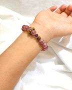 Pink natural stone bracelet with purple and gold accent beads worn on the wrist