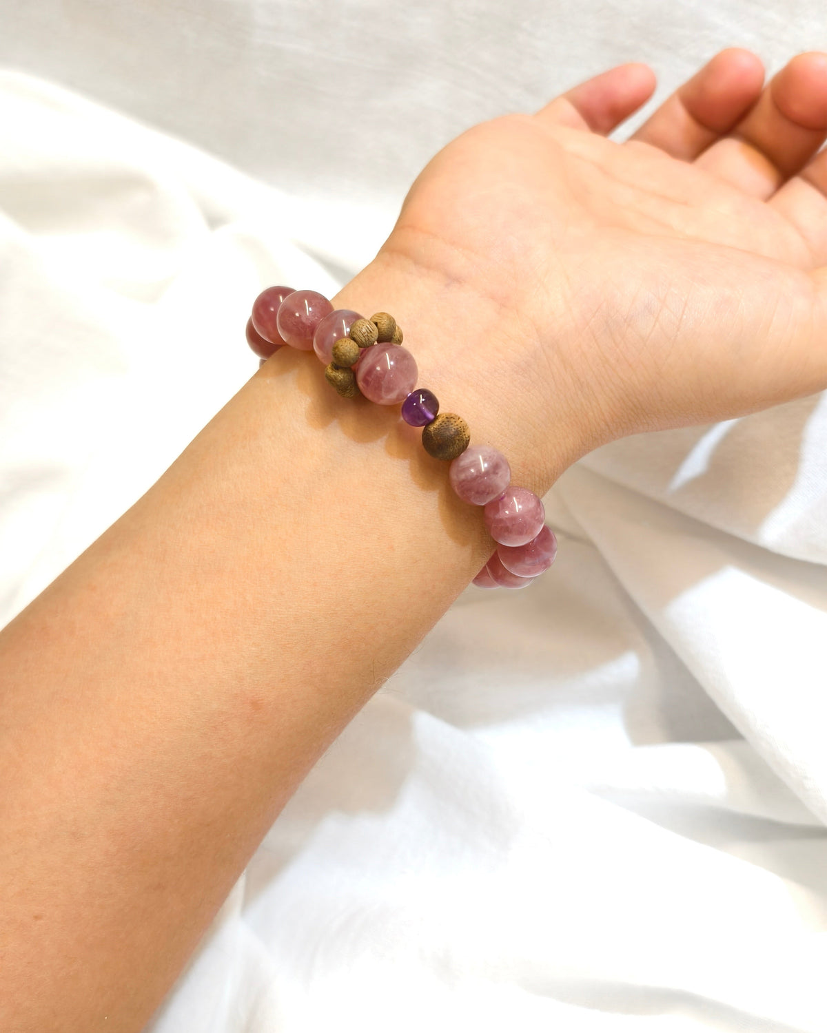Pink natural stone bracelet with purple and gold accent beads worn on the wrist