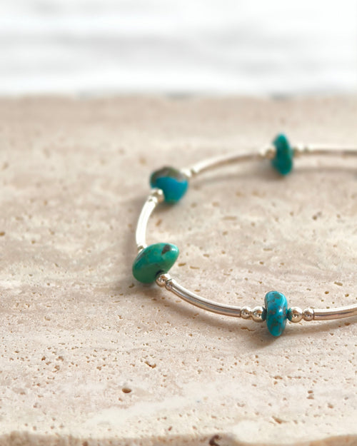 Close-up of turquoise tone stone beads with silver accents on a handmade bracelet